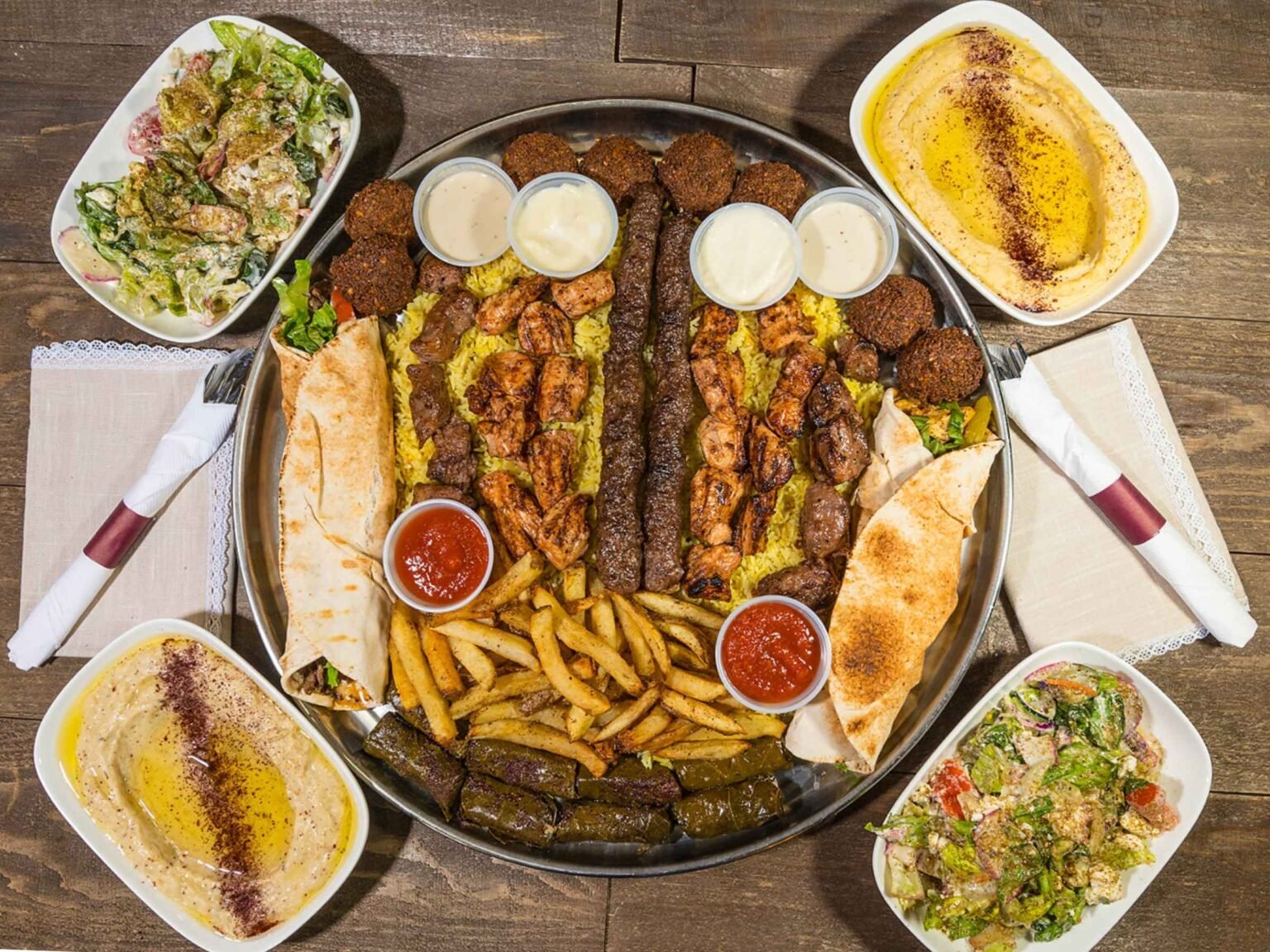 Lebanese family tray with grilled chicken, beef kebabs, falafel, hummus, grape leaves, fries, pita bread, and fresh salads served on a large platter.