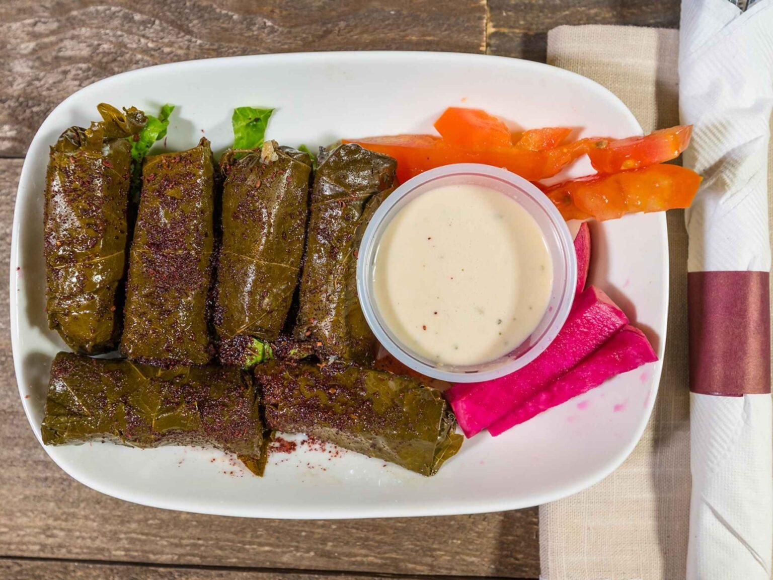 Lebanese stuffed grape leaves served at That Lebanese Place with tahini sauce, pickled turnips, and fresh tomato slices.