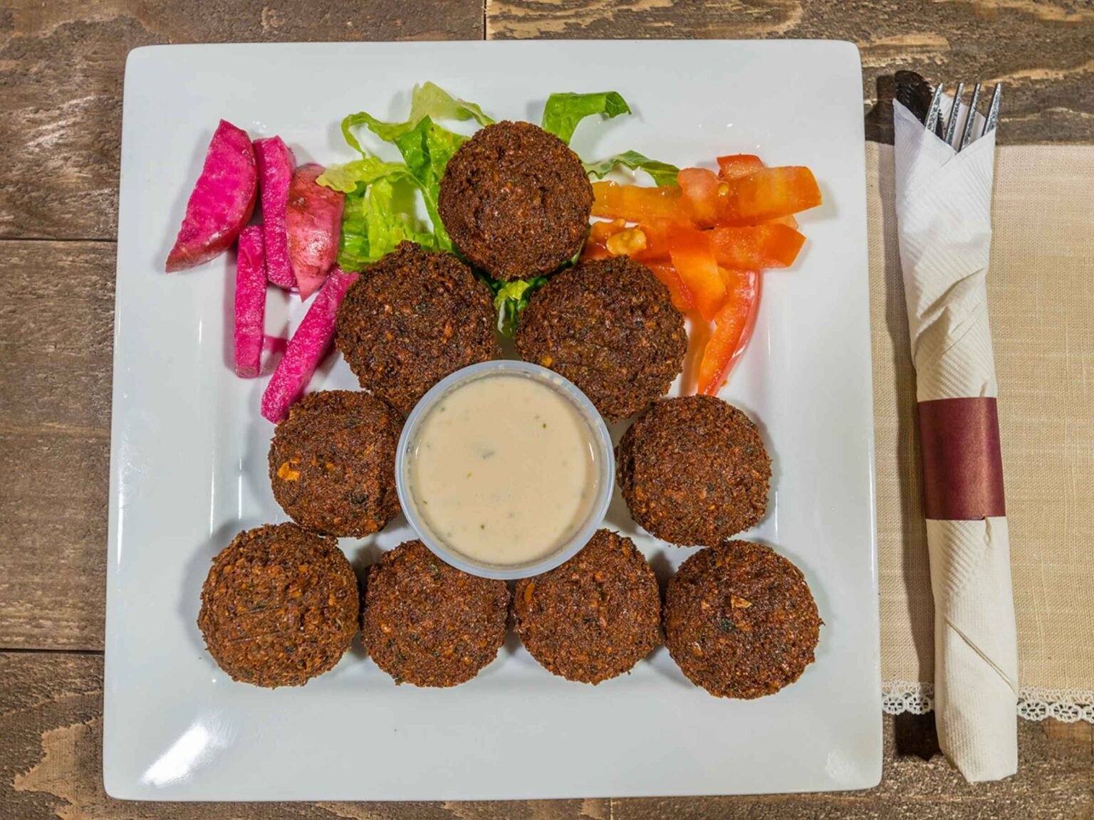 Crispy Lebanese falafel served at That Lebanese Place with tahini sauce, pickled turnips, vegetables, and fresh tomato slices.