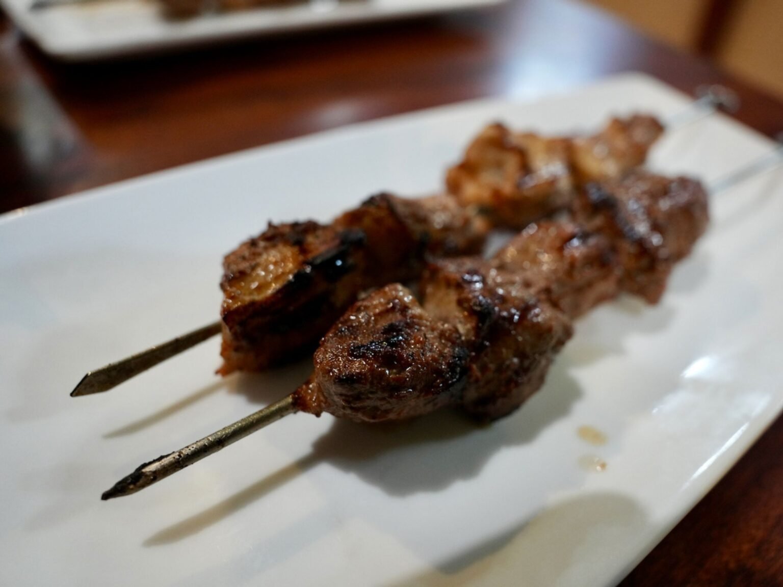 Two perfectly grilled Lebanese meat skewers served on a white plate at That Lebanese Place.