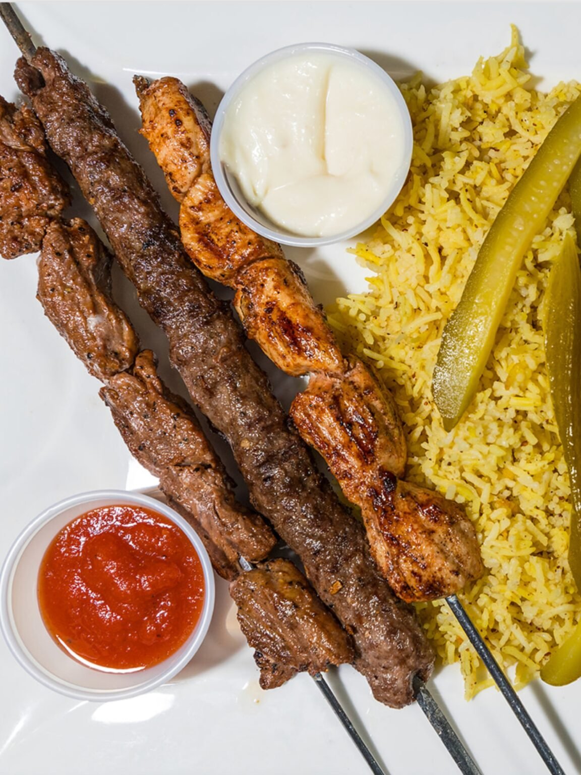 Mixed Grill Kabab plate from That Lebanese Place featuring chicken, beef, and kafta skewers served with basmati rice, homemade pickles, garlic sauce, and spicy red sauce.