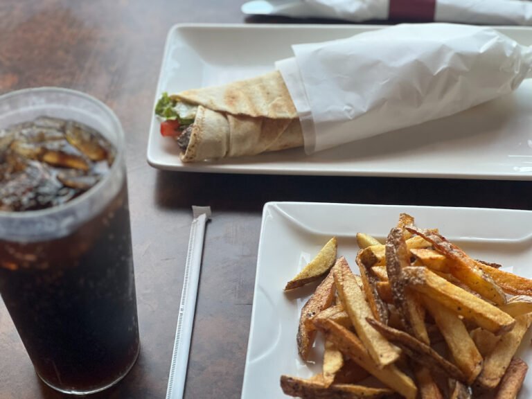 A freshly made Lebanese wrap served with golden fries and a soda on a rustic wood table at That Lebanese Place.
