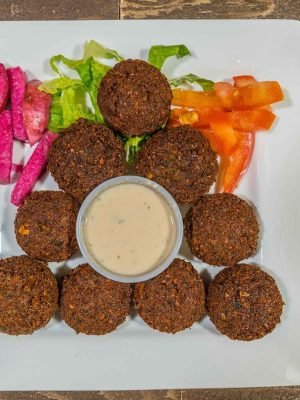 Crispy Lebanese falafel served at That Lebanese Place with tahini sauce, pickled turnips, vegetables, and fresh tomato slices.
